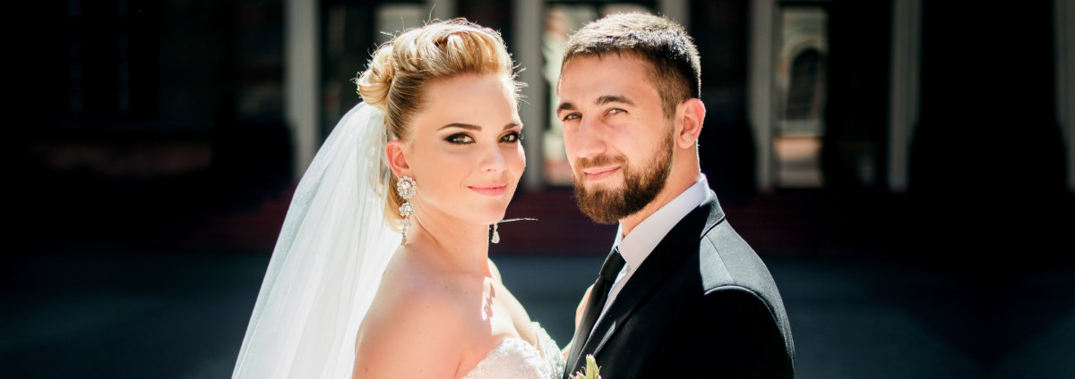 groom holds bride's waist tender while they pose on the pavement backyard